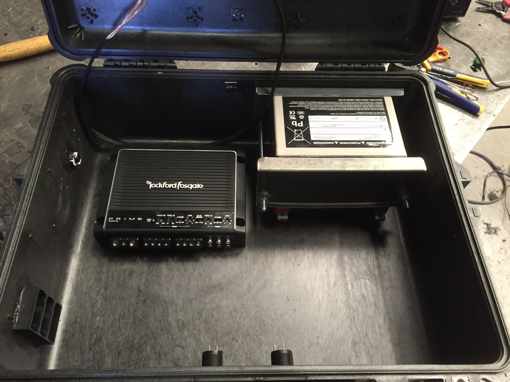 Interior side view of Pelican case showing amp, battery cradle, vent cutouts, and switch panel posts