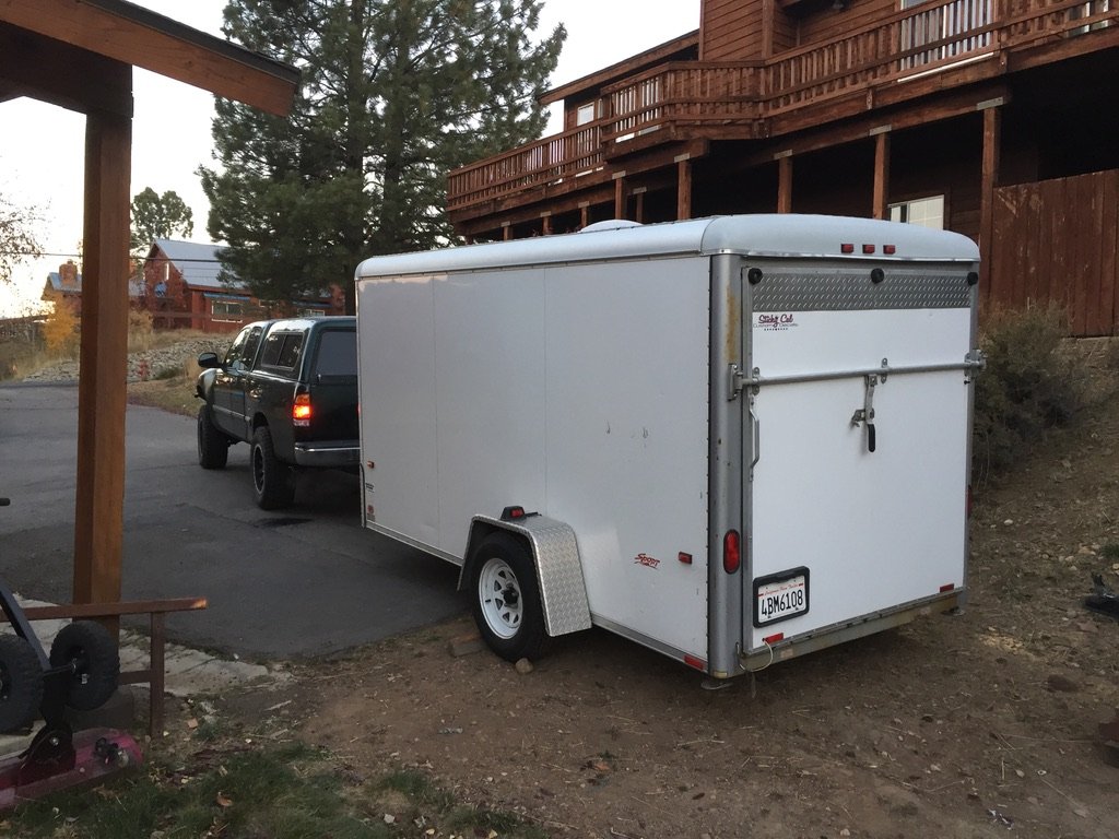 The trailer arrives home — white enclosed cargo trailer hitched behind a green Toyota Tacoma, parked beside the Truckee house at dusk, October 2017