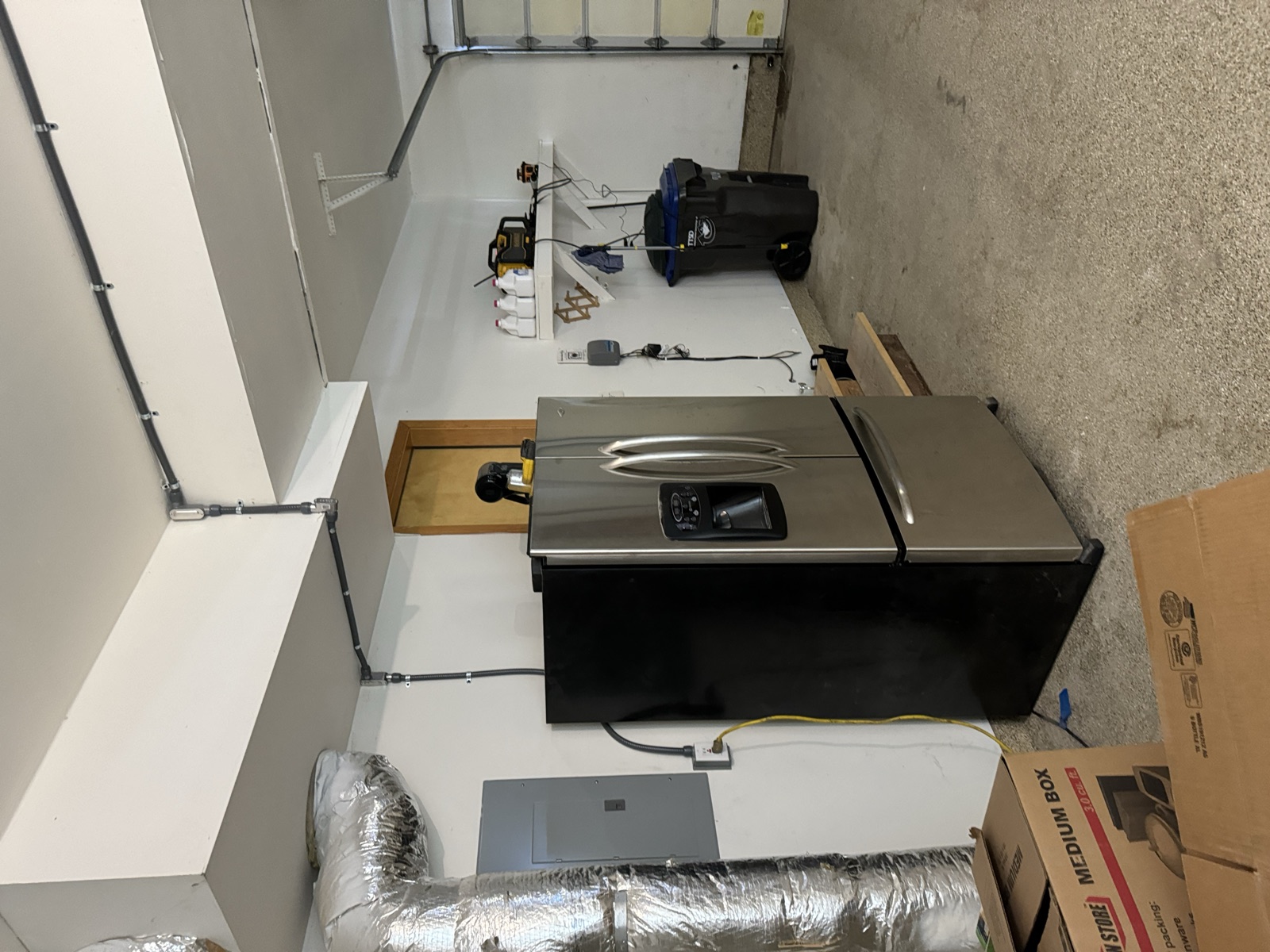 Empty white-painted two-bay garage in February 2024 with table saw centered on the concrete floor, electrical conduit roughed in, no cabinets yet