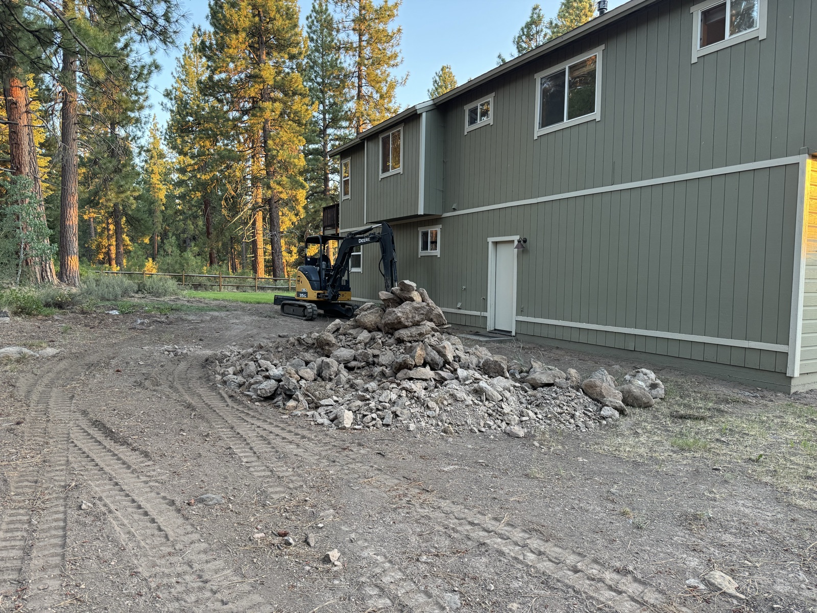Mini excavator regrading the driveway approach next to the home in late summer