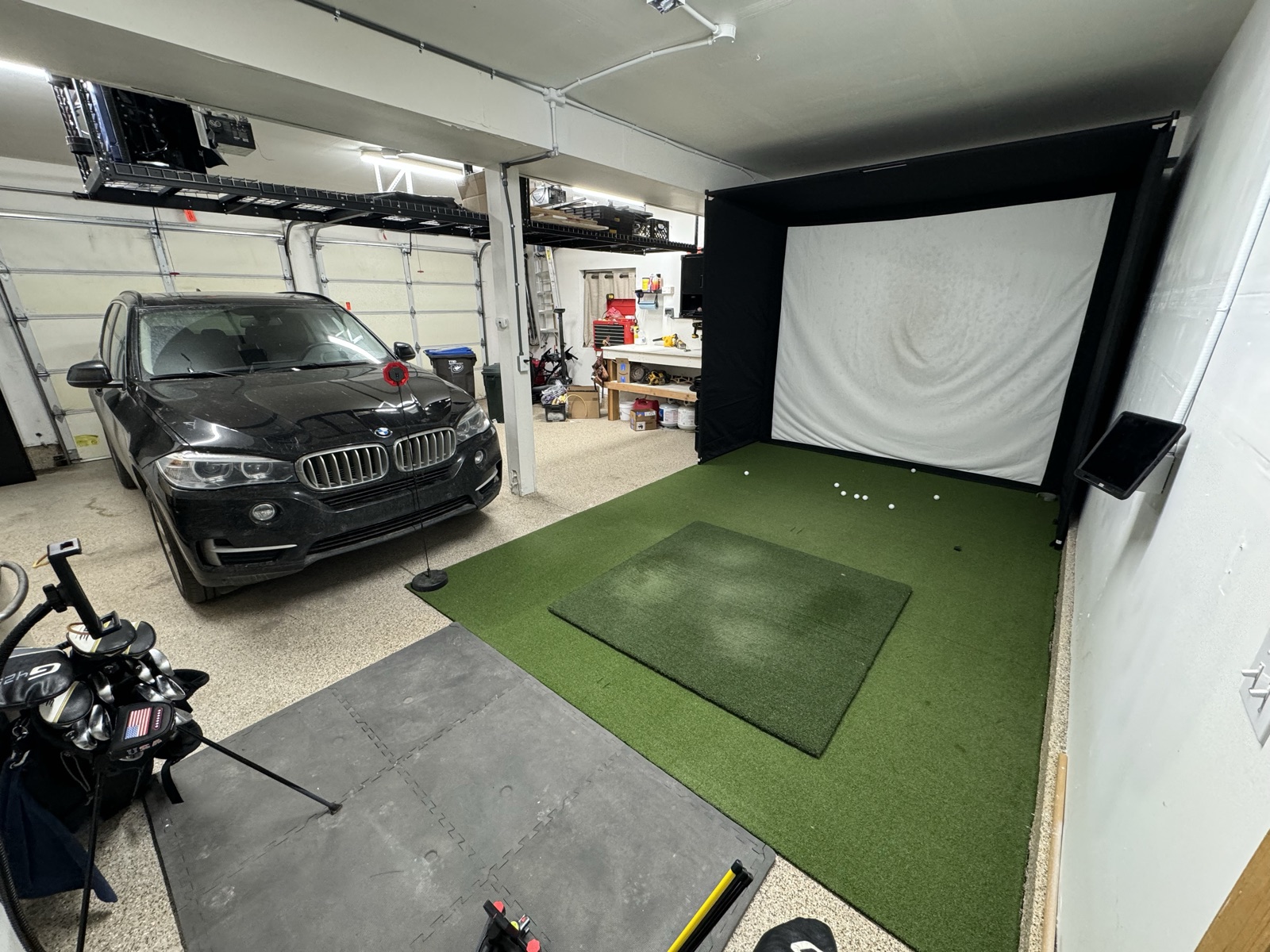 Reveal cinematic — BMW parked in the left bay with the golf simulator bay visible to the right, overhead storage above