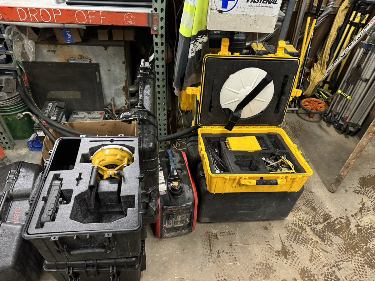 GPS base and rover equipment in open hard cases in the shop — antennas, receivers, and cables in foam