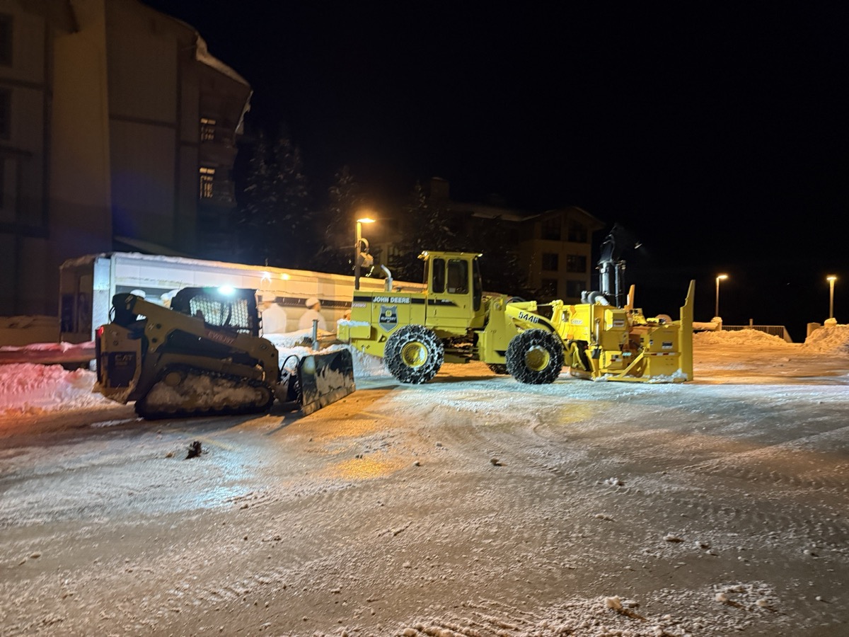 CAT track loader with a snow pusher and John Deere loader with a blower attachment staged at night at Palisades Tahoe Village