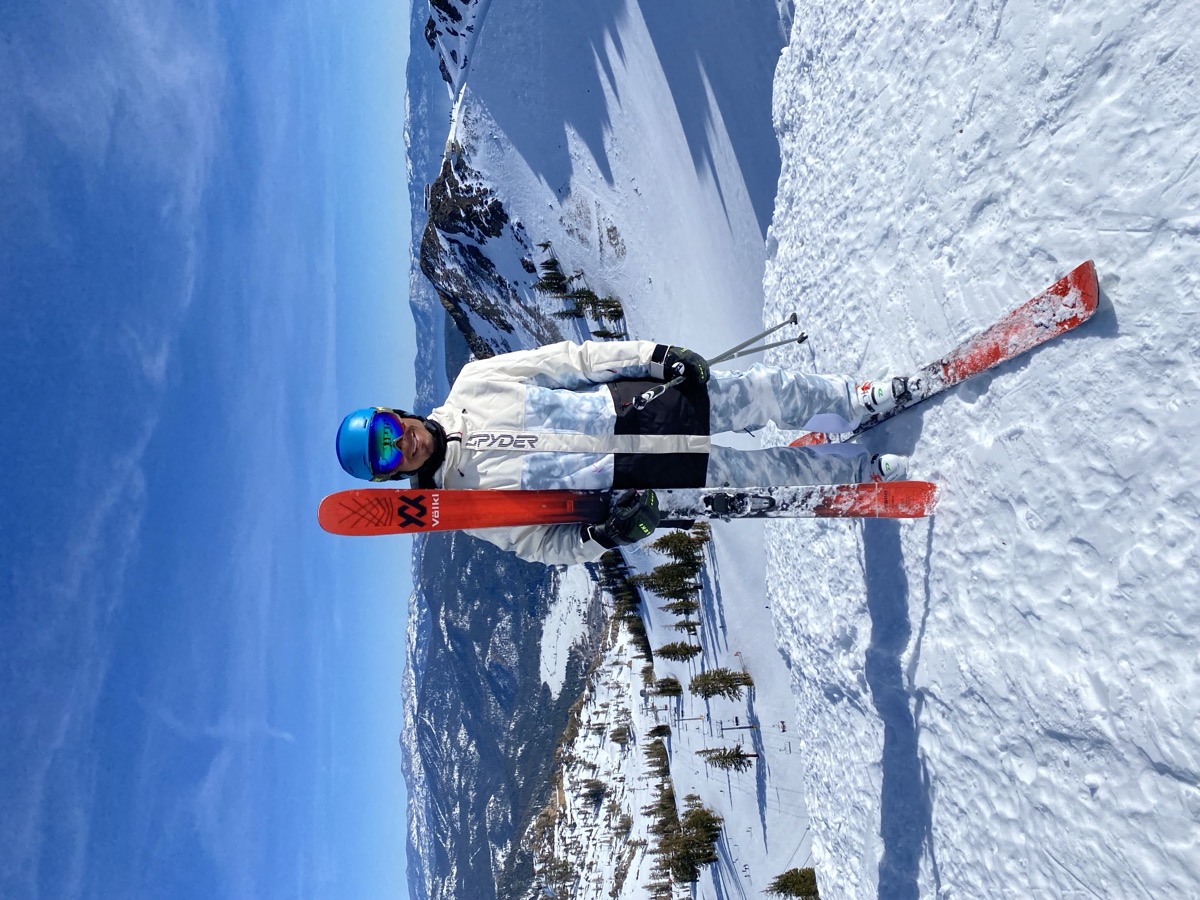 Errol standing at the summit of Palisades Tahoe holding Volkl skis with the Sierra Nevada panorama behind him