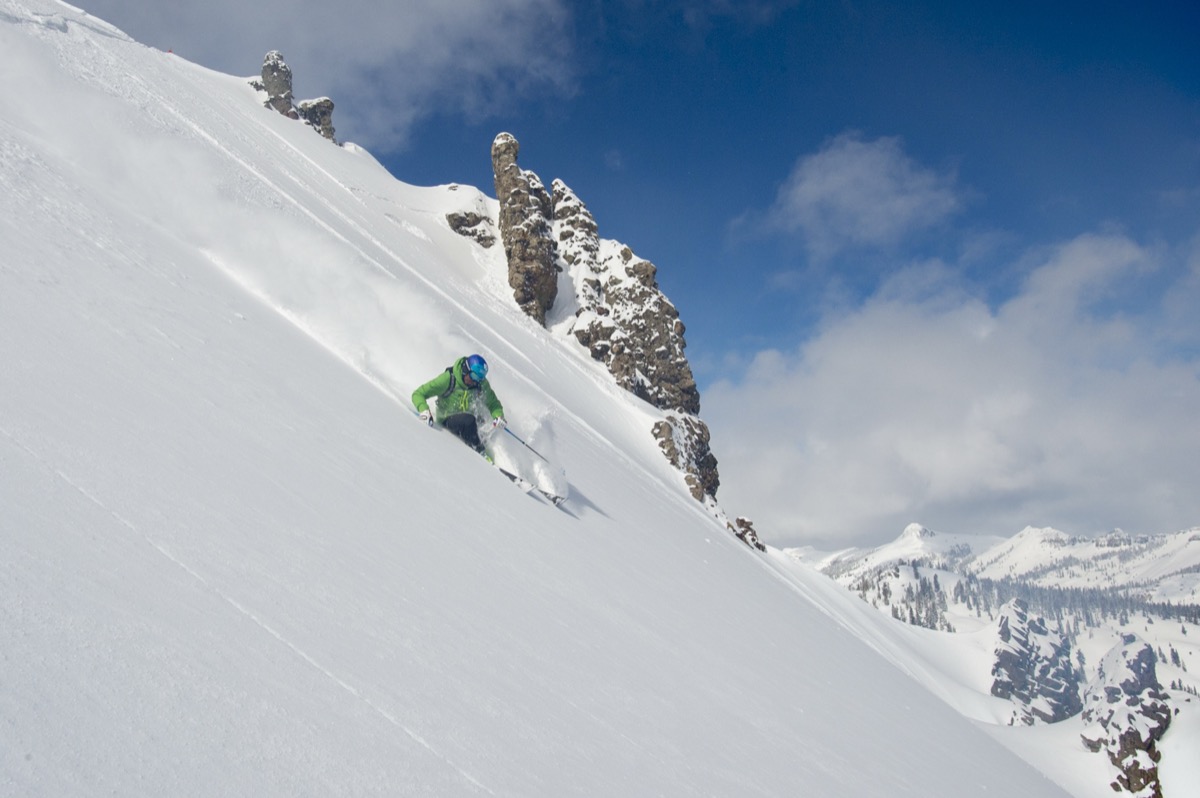 Errol charging steep powder beneath a rock spire on a bluebird day