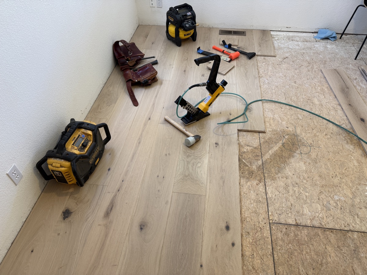 Mid-install hardwood floor at the halfway mark with DeWalt nailer, radio, and tools
