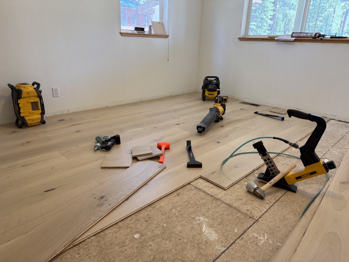 Mid-install hardwood floor with full DeWalt tool spread and mountain views through windows