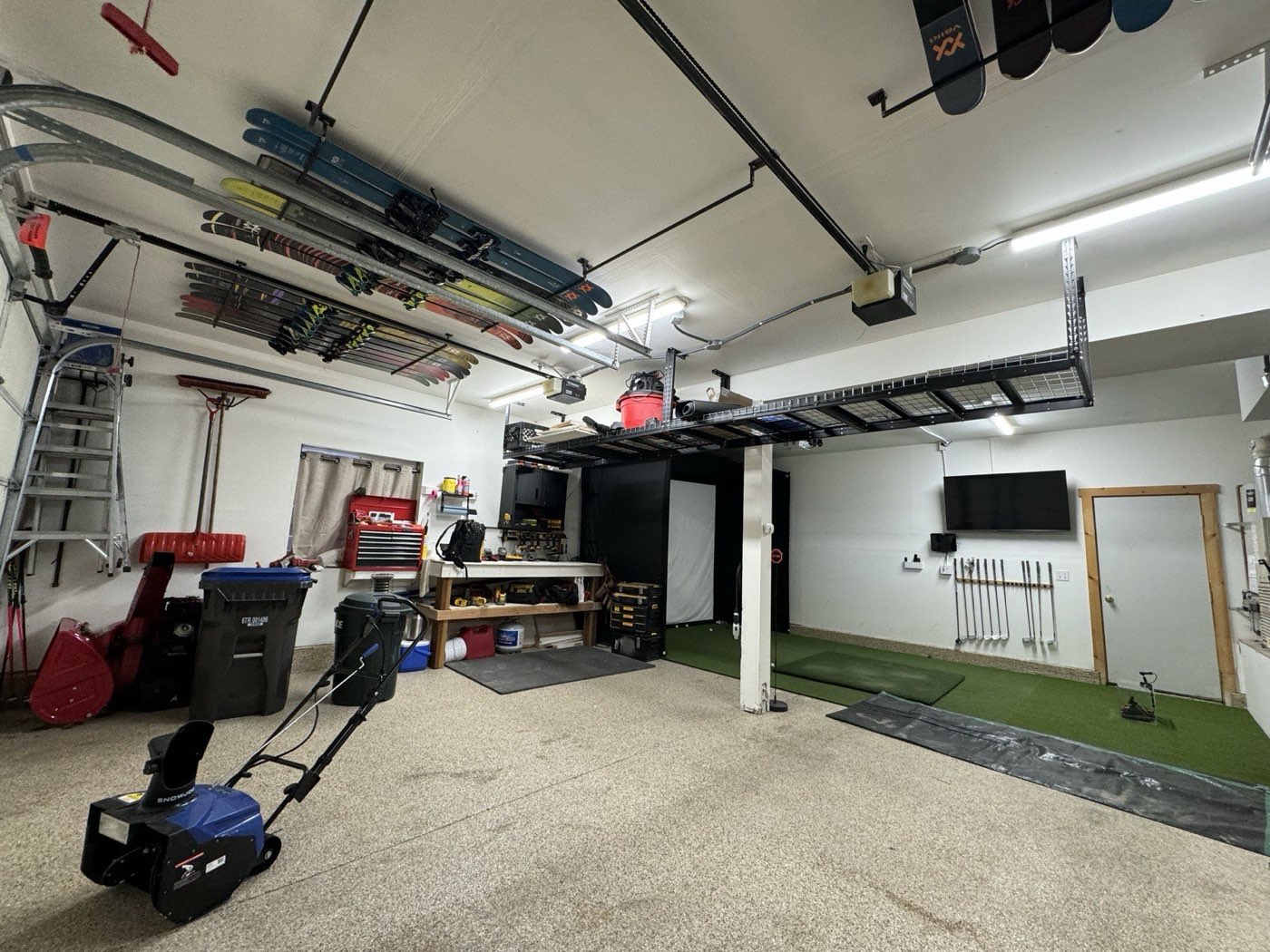 Wide panoramic view of garage with skis on ceiling and golf simulator