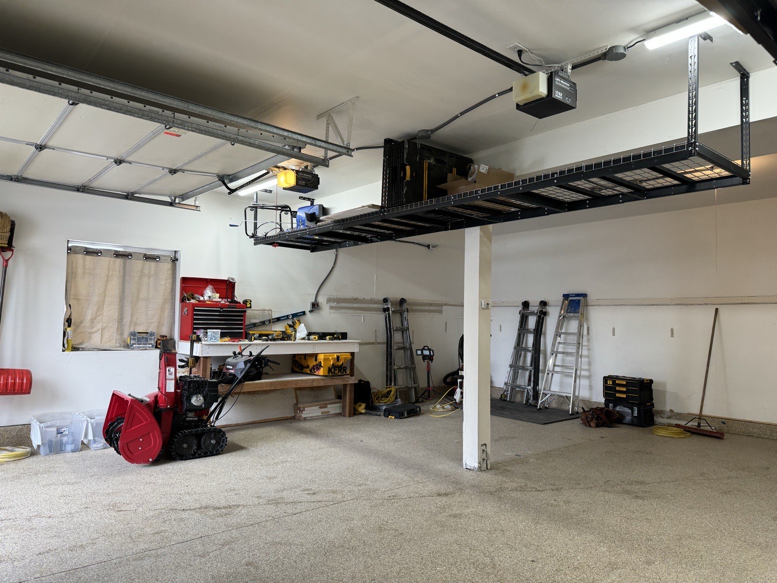 Overhead storage platform, workbench, and track-drive snowblower in a cleared garage bay