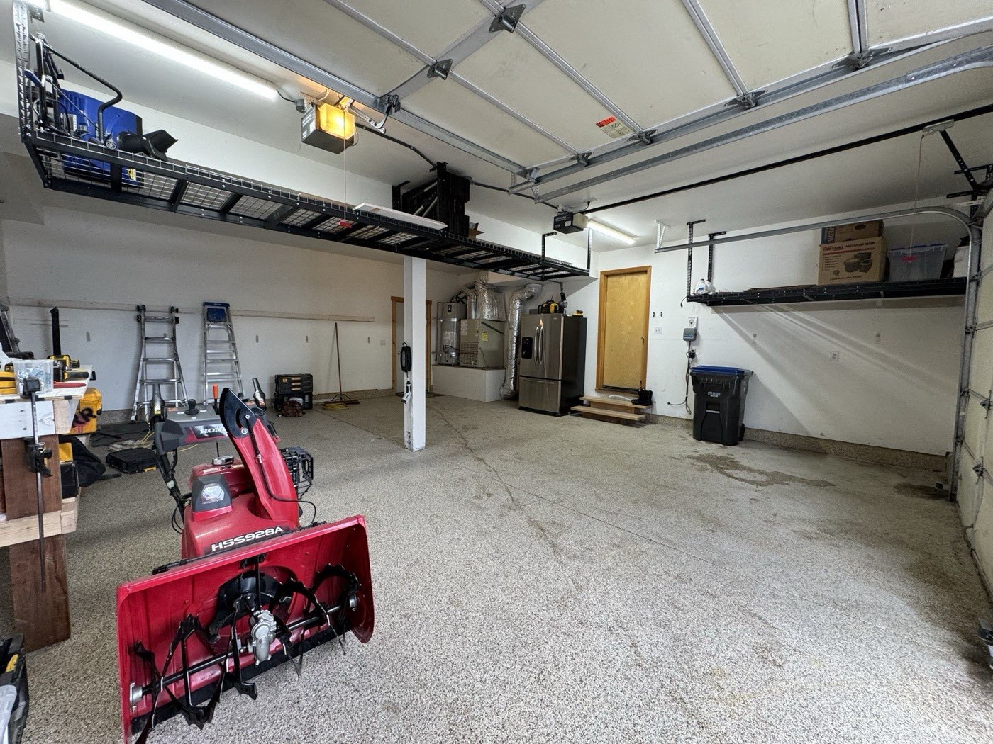Honda track-drive snowblower parked on a clear floor beneath overhead storage platforms