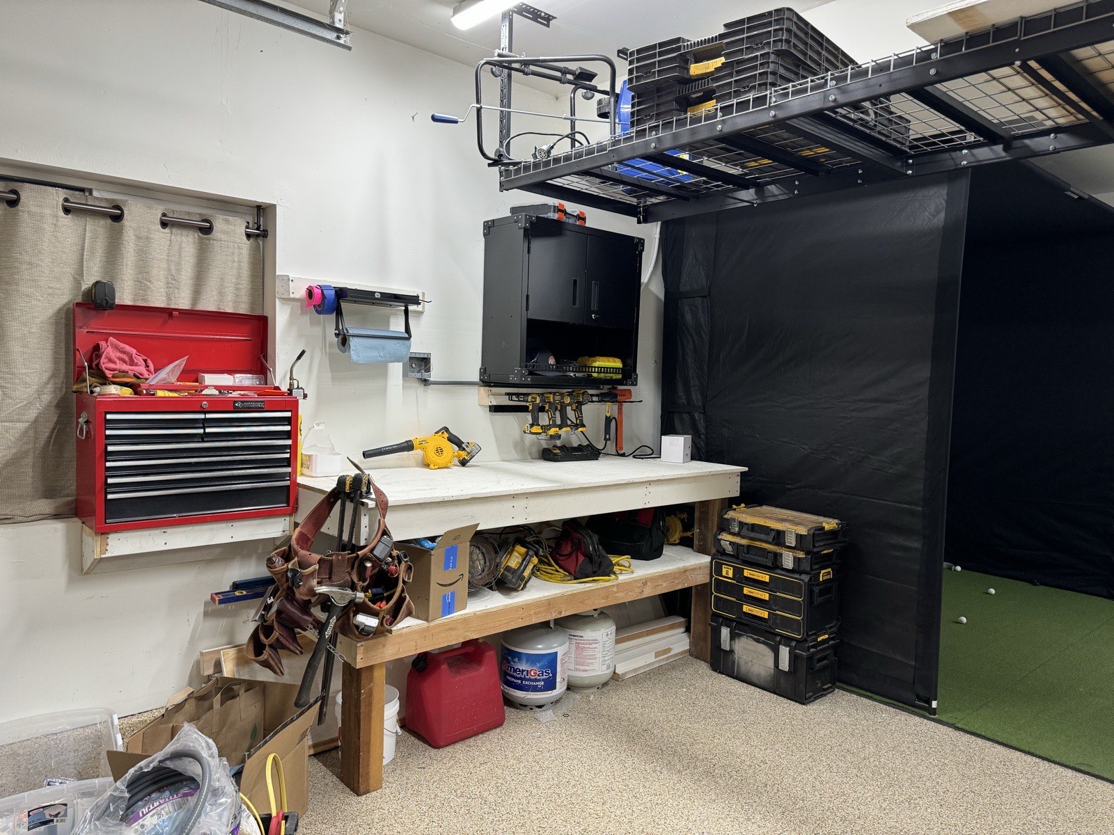 Workbench with wall-hung tool chest, drill rack, and stacked toolboxes beside the golf-sim enclosure